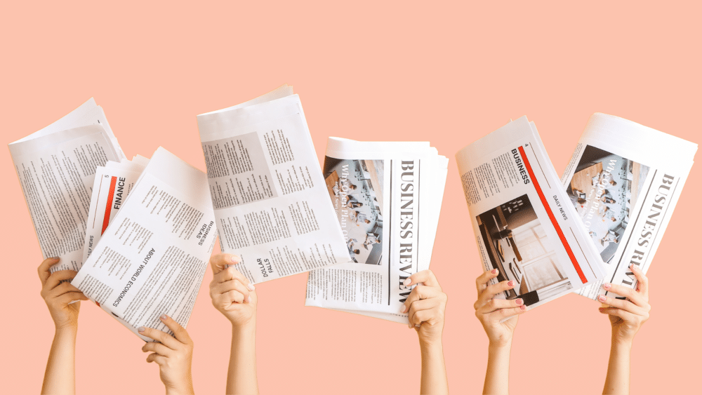 Image of hands holding trade press newspapers with a pink background